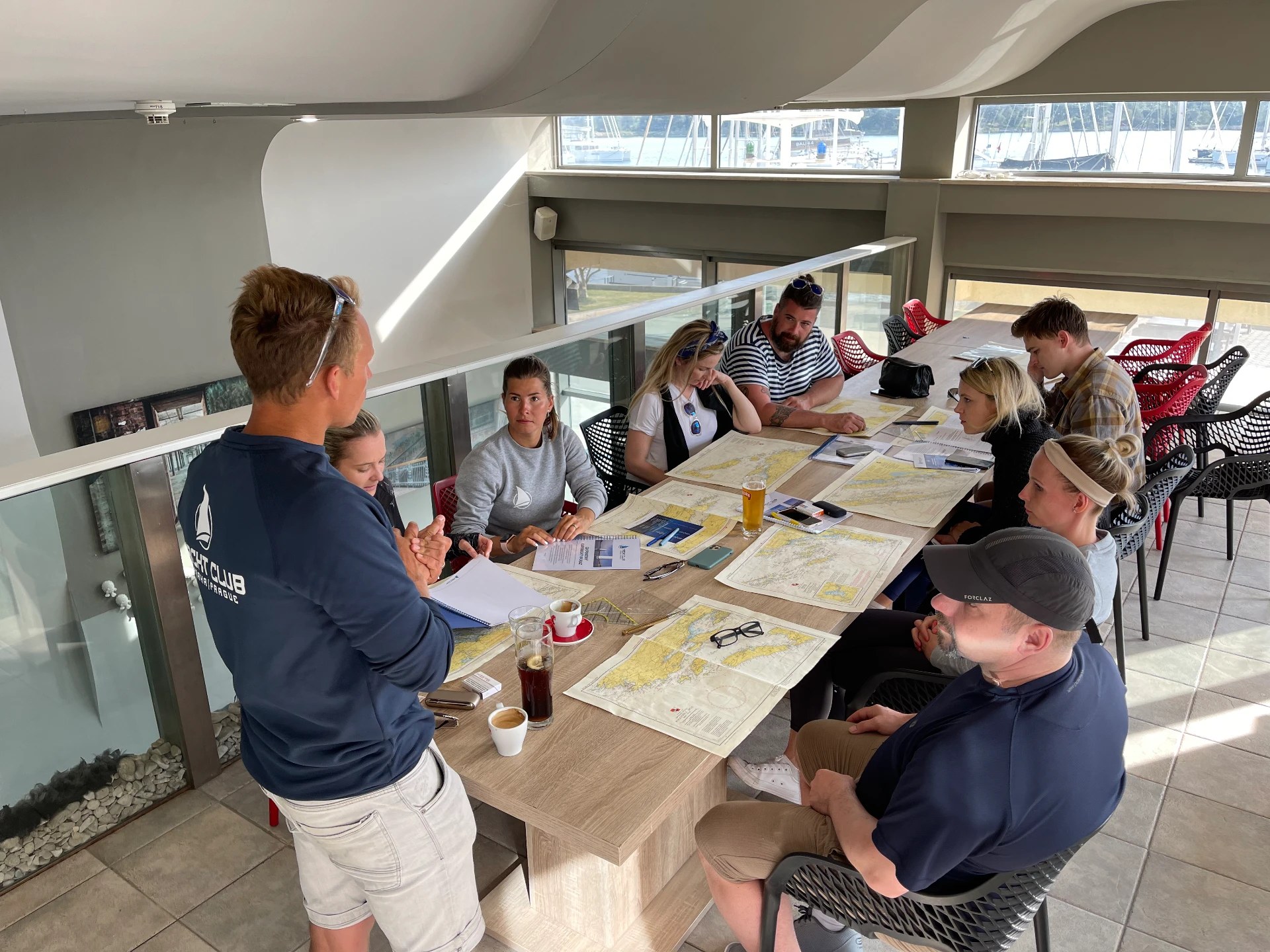 Instructor explaining the passage plan to the crew at the table with nautical charts